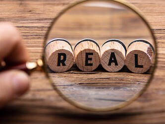 magnifying glass looking at word REAL spelled on wooden blocks
